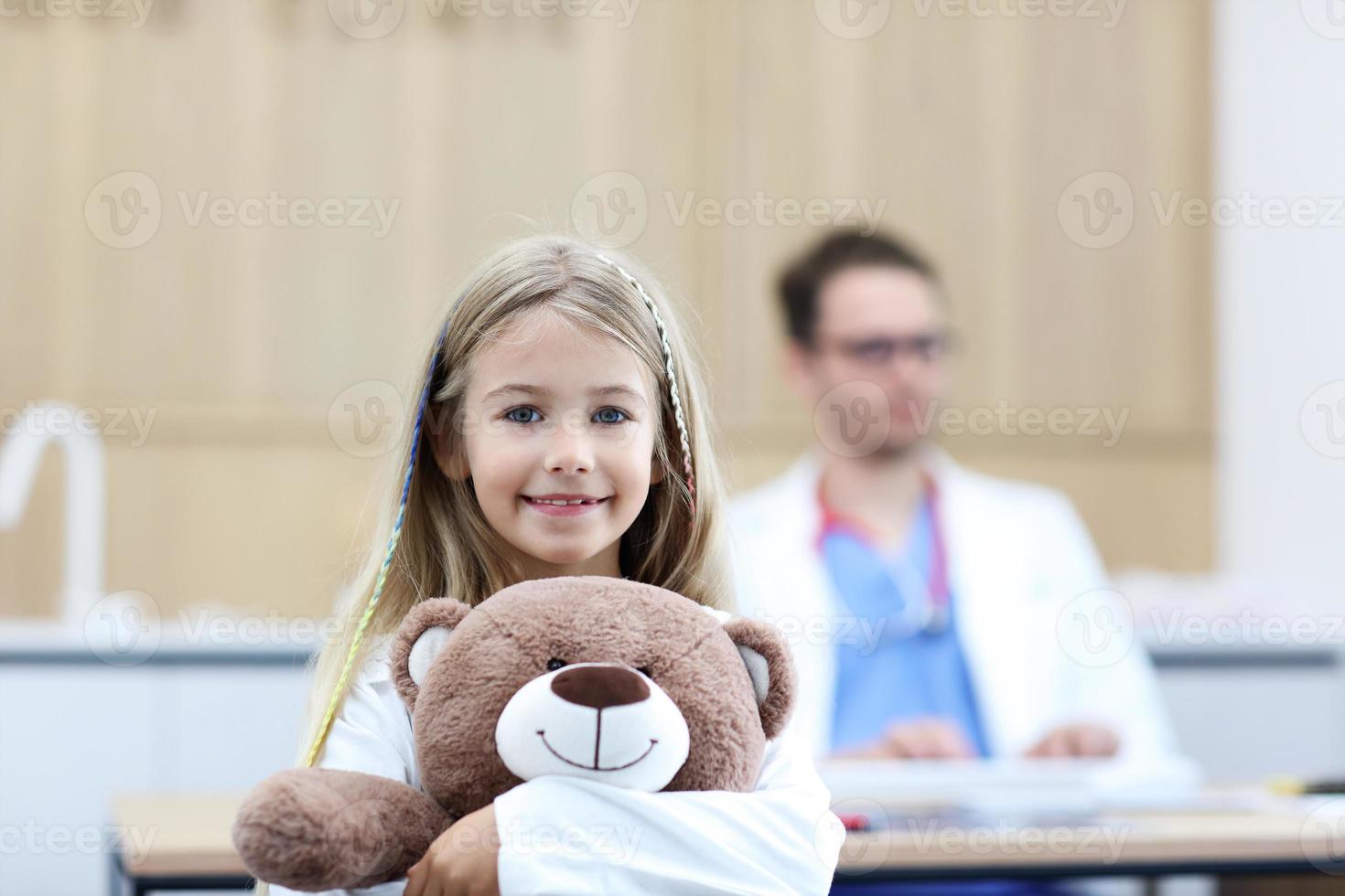 weinig meisje in kliniek met kinderarts in de achtergrond foto