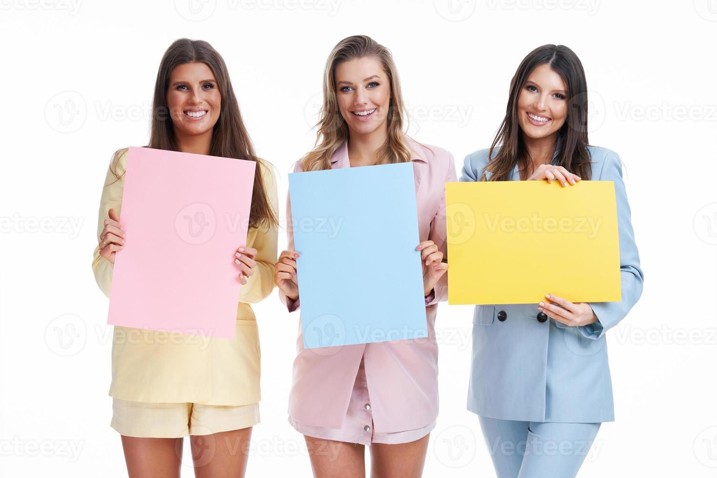 drie Dames in pastel pakken Holding aanplakbord poseren over- wit achtergrond foto