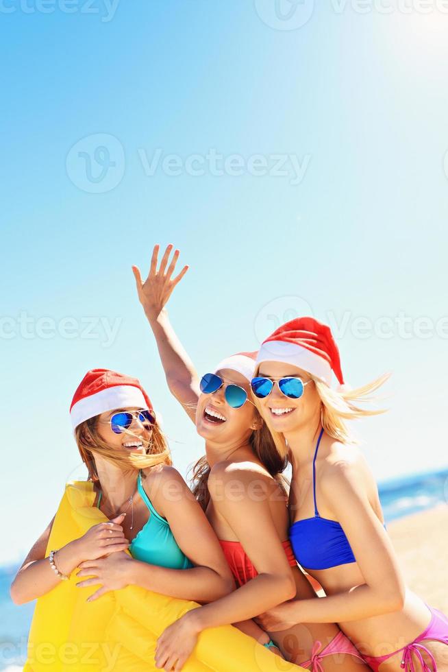 groep van meisjes in santa's hoeden hebben pret Aan de strand foto