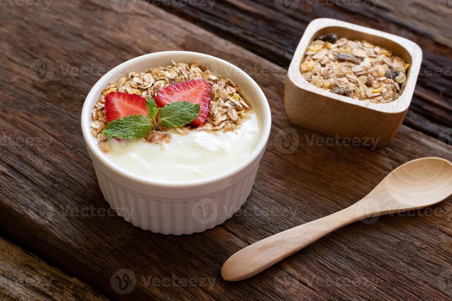 aardbei yoghurt in een houten kom met muesli, honing, munt en vers aardbei Aan houten achtergrond. Gezondheid voedsel concept. foto