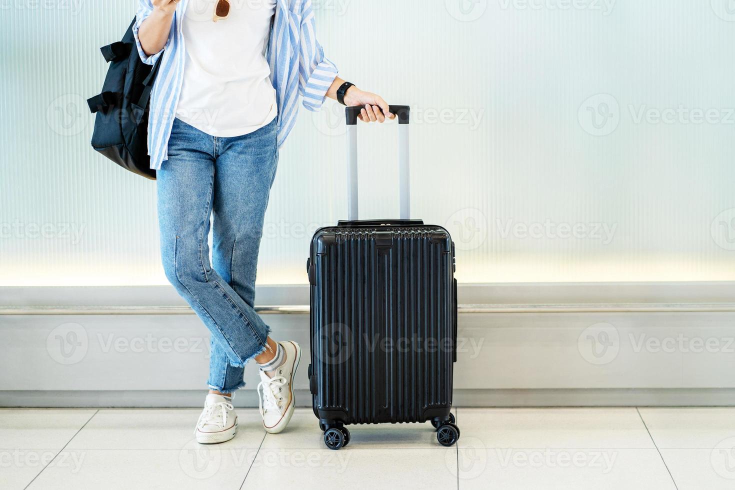 Aziatisch vrouw tiener gebruik makend van smartphone Bij luchthaven terminal staand met bagage koffer en rugzak voor reizen in vakantie zomer foto