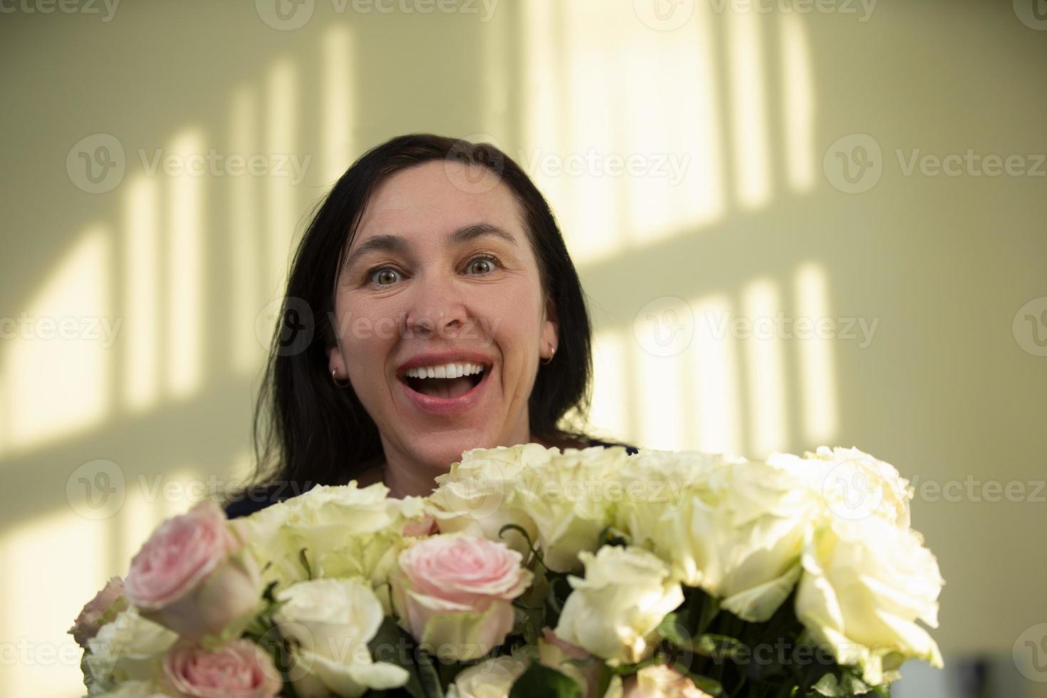 portret van een positief charmant vrolijk ouderen vrouw wie ontvangt een boeket van rozen, verheugt zich, geniet de viering van maart 8 of een verjaardag. foto