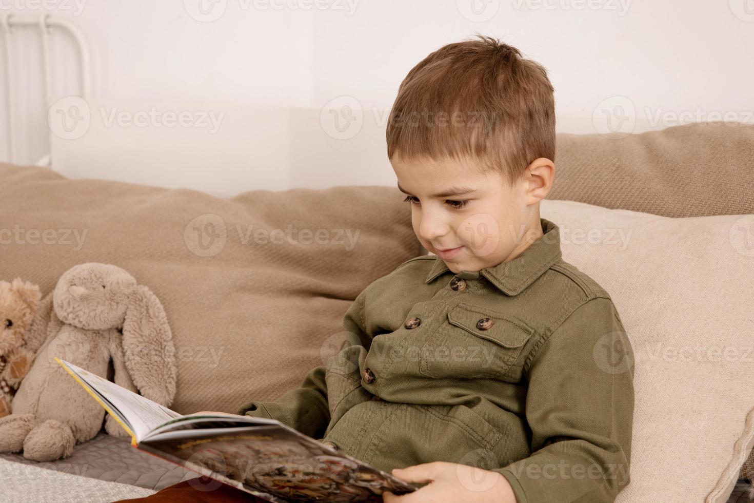 weinig en schattig Kaukasisch jongen lezing een boek Aan de bed Bij huis. interieur en kleren in natuurlijk aarde kleuren. knus omgeving. kind leest een fee verhaal. foto