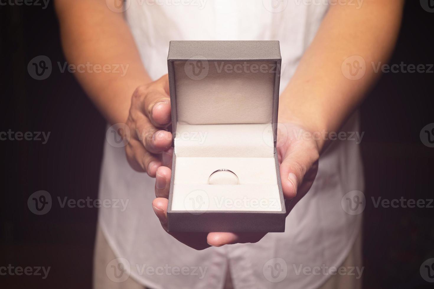 uitbreiden de hand- Holding de klein doos, geopend een wit goud ring met een klein diamant. gegeven Aan belangrijk dagen of huwelijk voorstellen foto