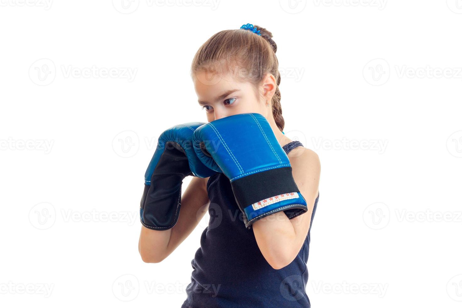 weinig meisje met varkensstaart staat in de groot blauw boksen handschoenen in voorkant van een camera foto