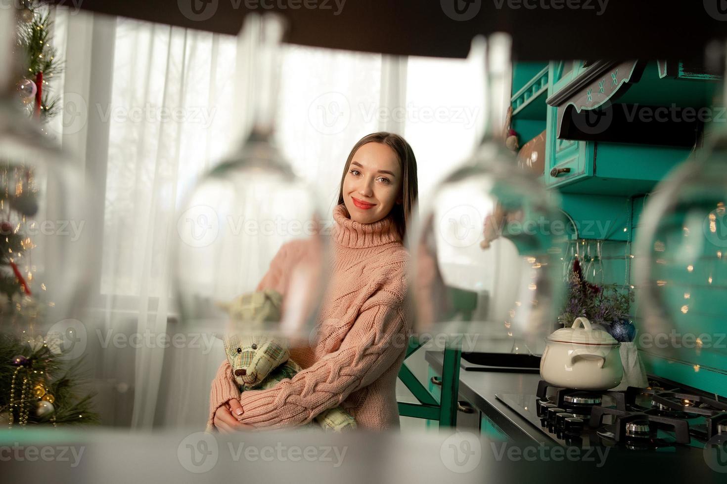 schattig vrouw glimlacht Aan camera Bij de keuken met beer in handen foto