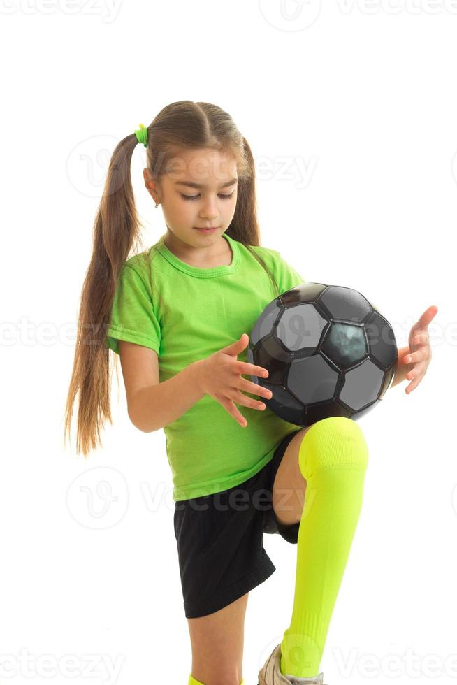 weinig blond meisje in sport uniform spelen met voetbal bal foto