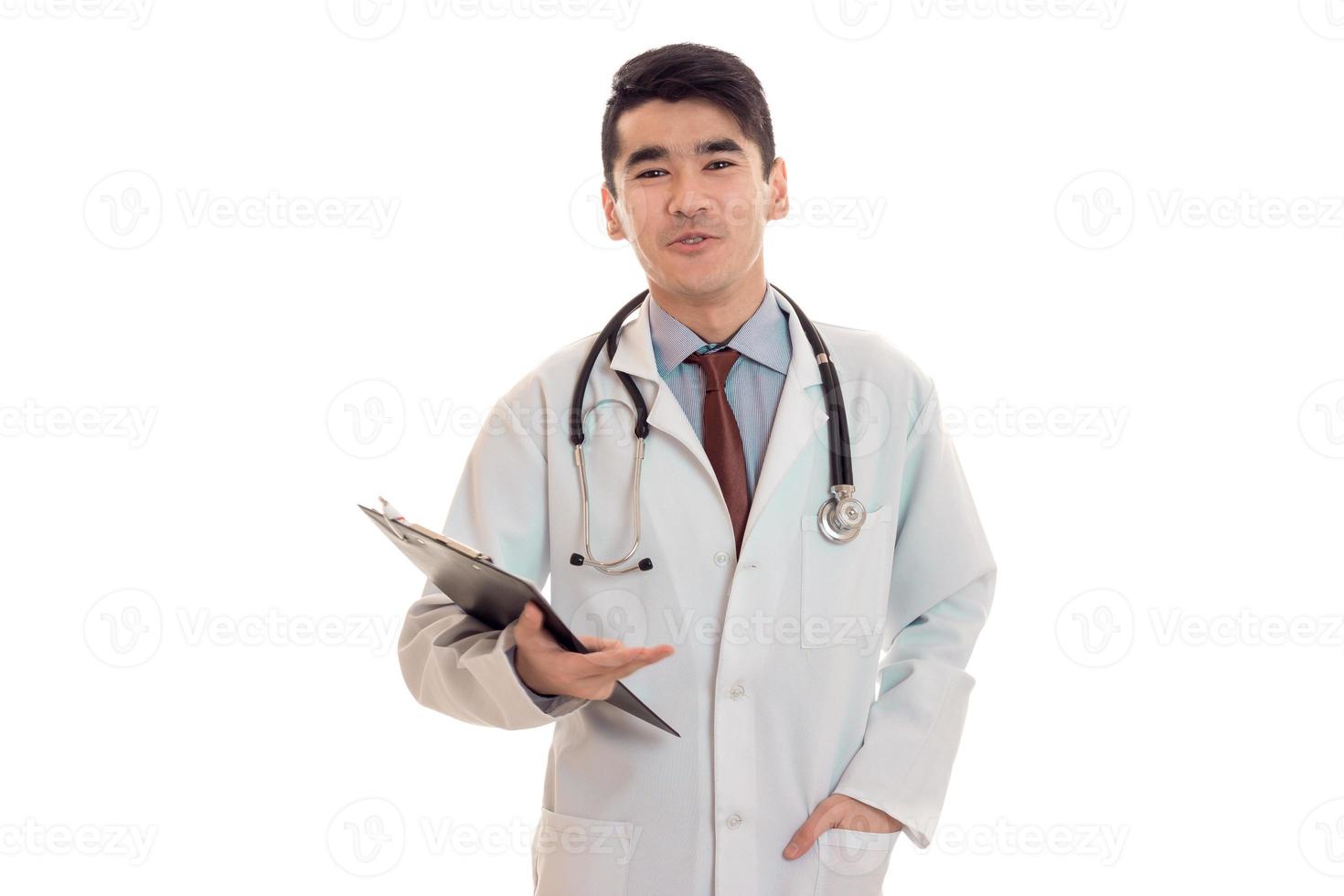 grappig jong brunette Mens dokter in wit uniform met stethoscoop op zoek Bij de camera geïsoleerd in studio foto