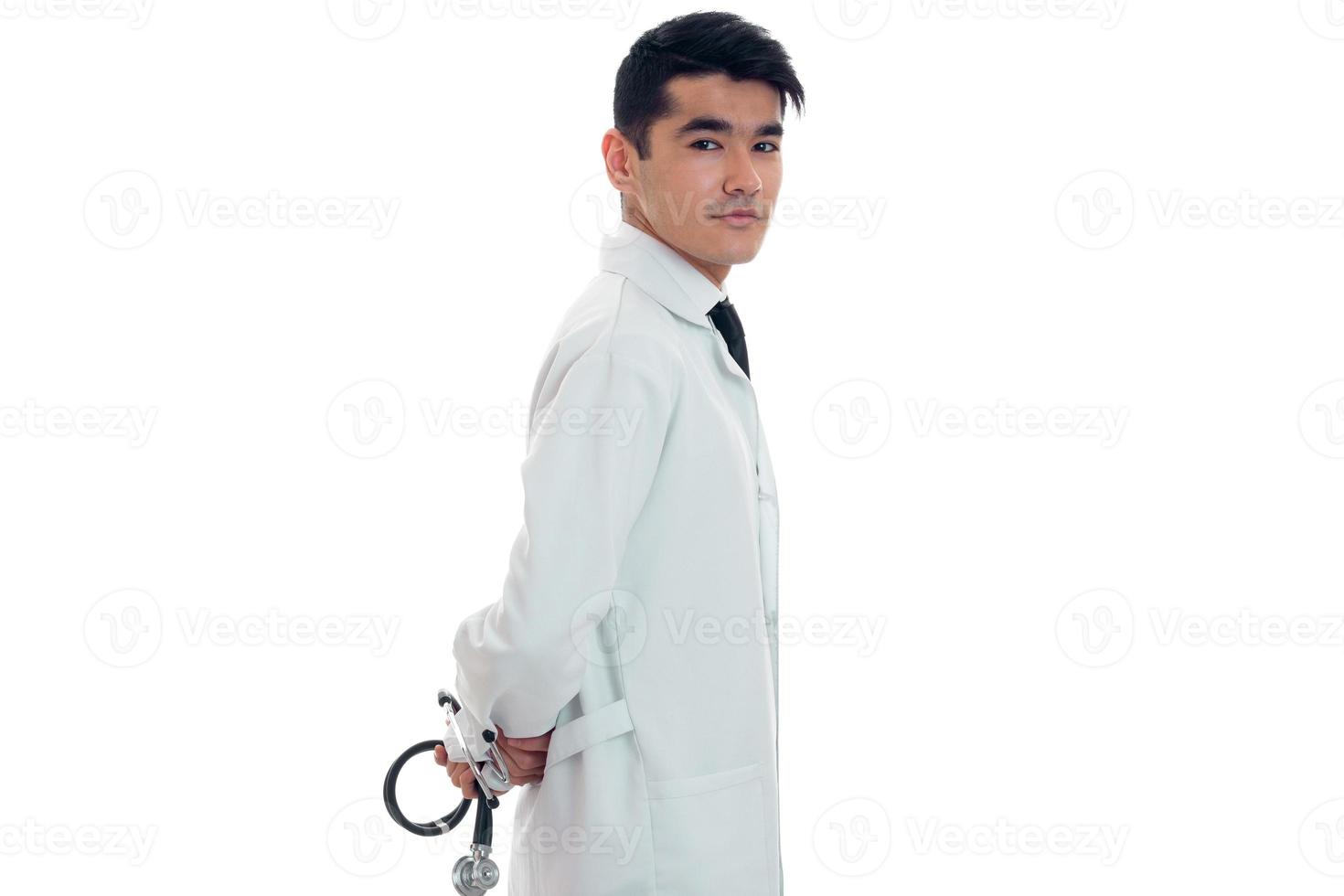 jong volwassen brunette Mens dokter in uniform met stethoscoop in zijn handen poseren Aan camera geïsoleerd Aan wit achtergrond foto