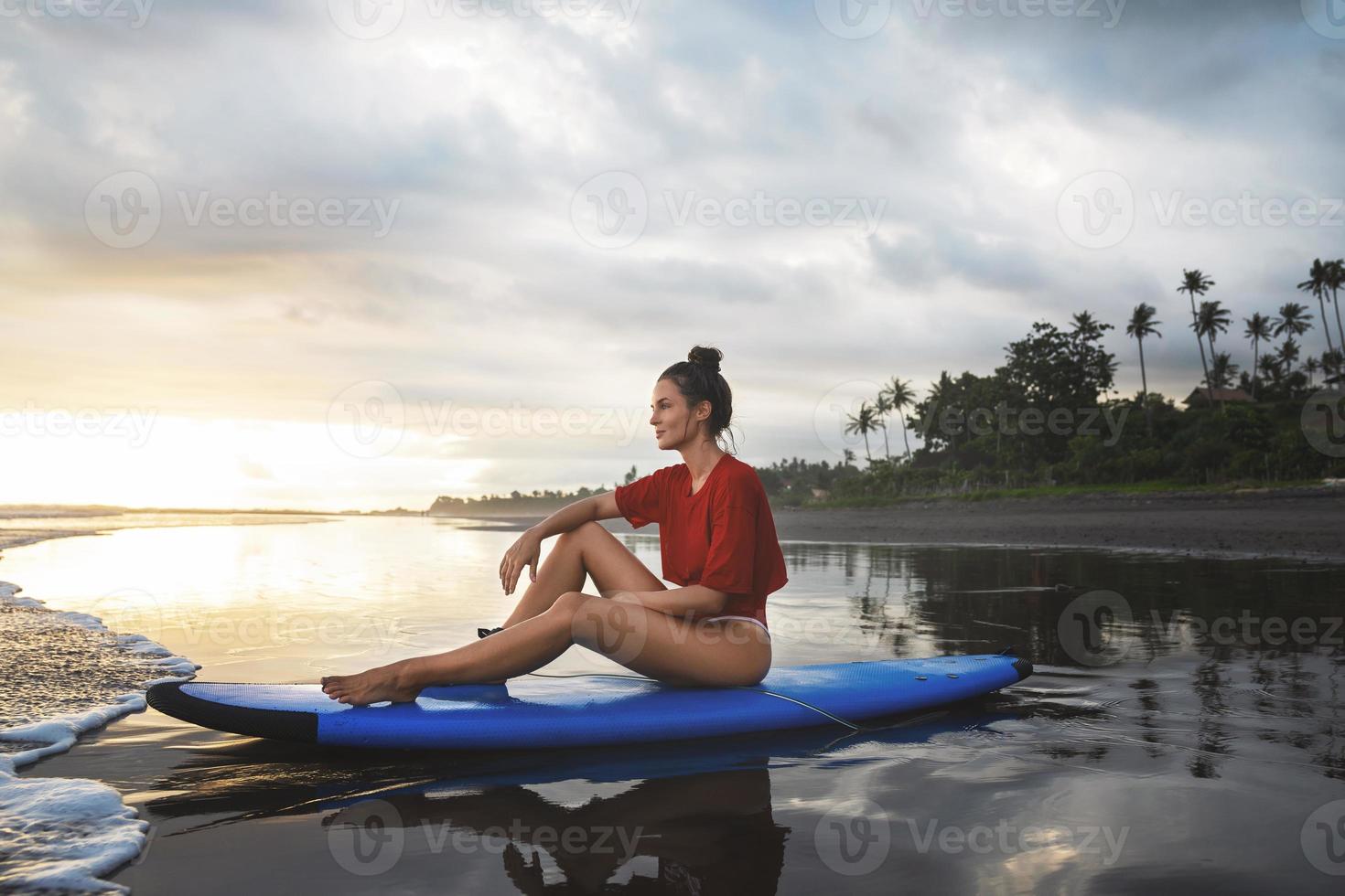 vrouw zittend Aan surfboard Aan de strand na haar surfing sessie foto