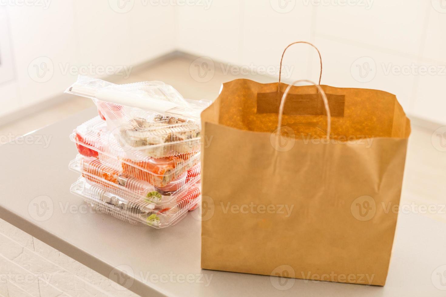 sushi broodjes in plastic doos in de buurt papier pakket Aan wit tafel. levering. nemen weg. foto