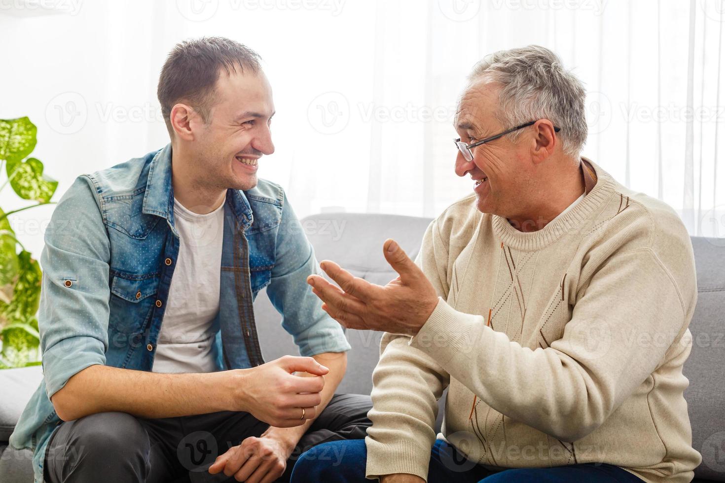 glimlachen gegroeid zoon zitten Aan bankstel kom tot rust met senior vader praten sharing gedachten op zoek in ogen, gelukkig millennial Mens rust uit Aan sofa spreken met ouderen vader genieten vrije tijd familie weekend Bij huis. foto