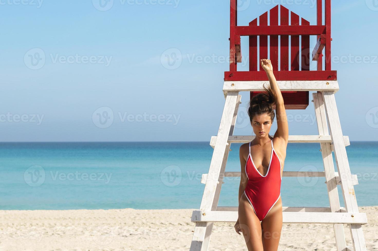 sexy vrouw in rood zwempak poseren naast een badmeester toren foto