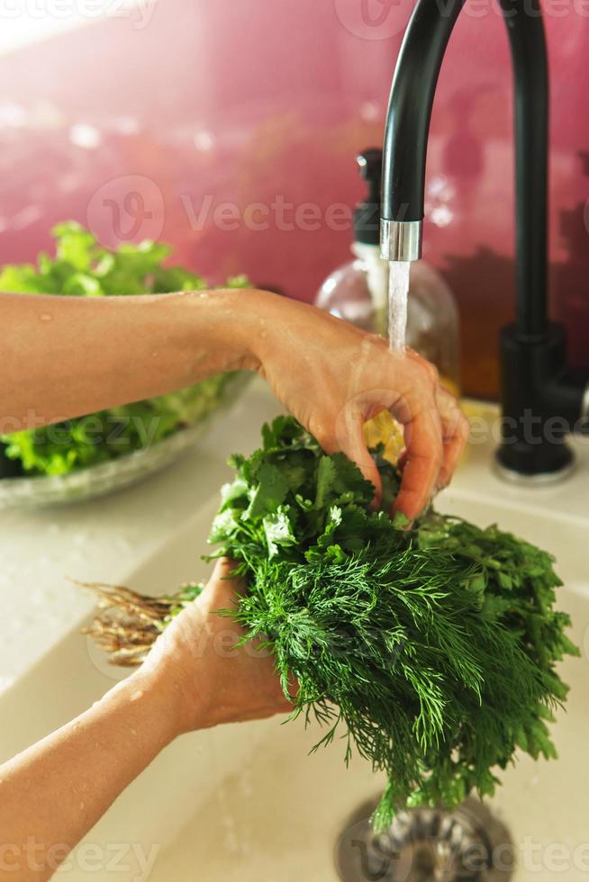 vrouw handen het wassen dille en peterselie in de kraan water foto