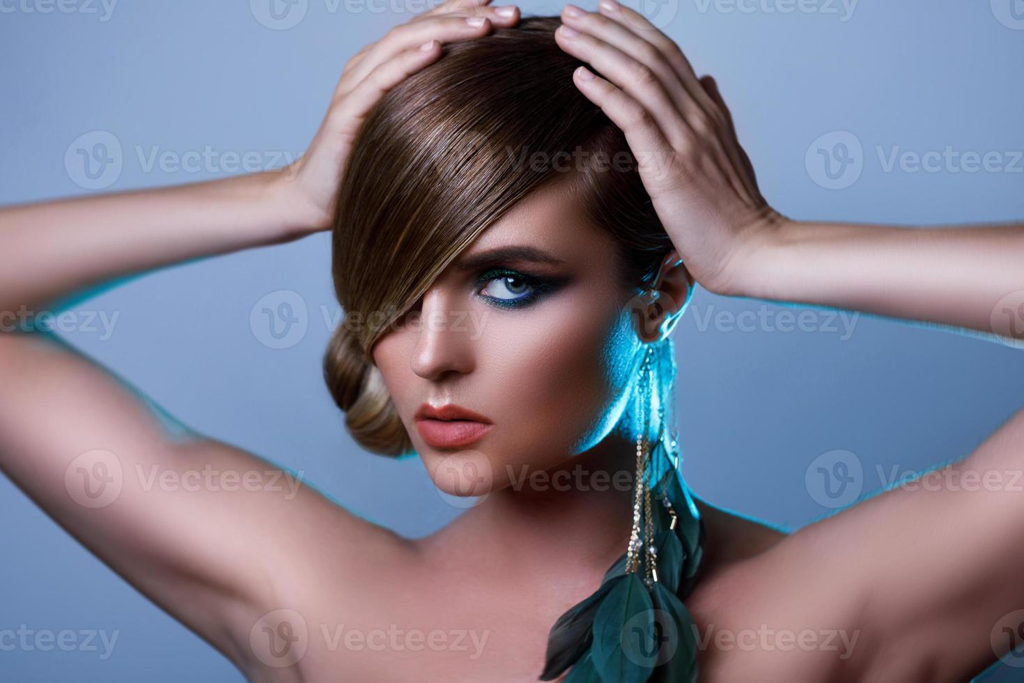 model- in elegant beeld met strak haar- aan het bedekken een oog en veer oorbel foto