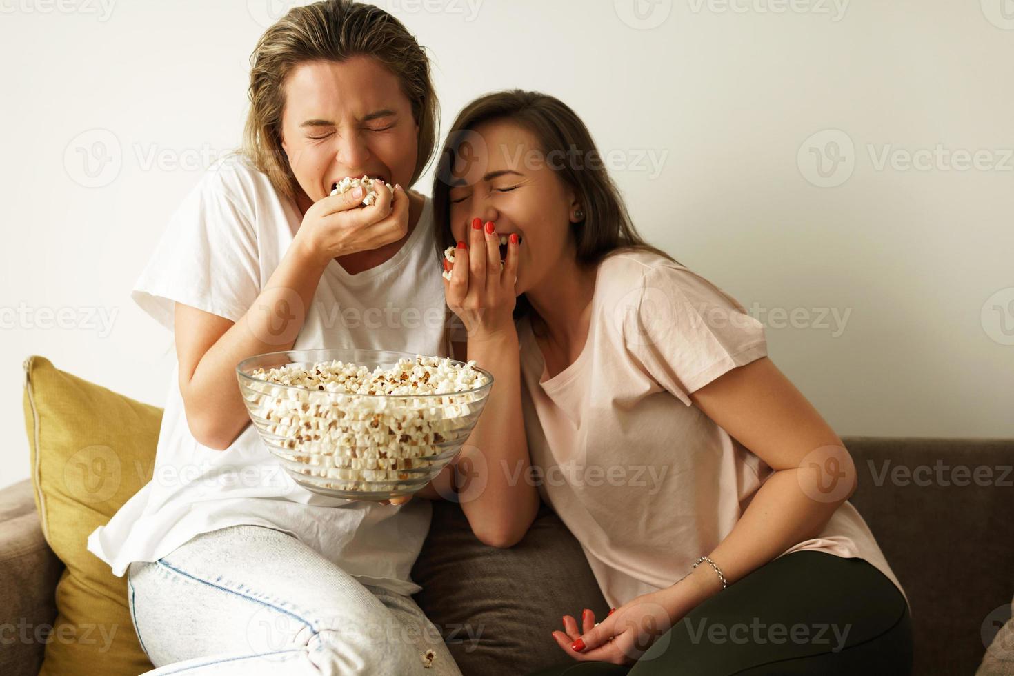 twee mooi vriendinnetjes aan het kijken TV tonen en aan het eten popcorn foto