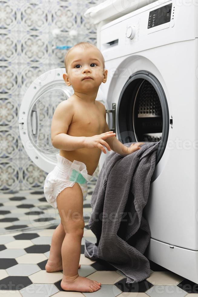 schattig baby jongen naast de het wassen machine foto