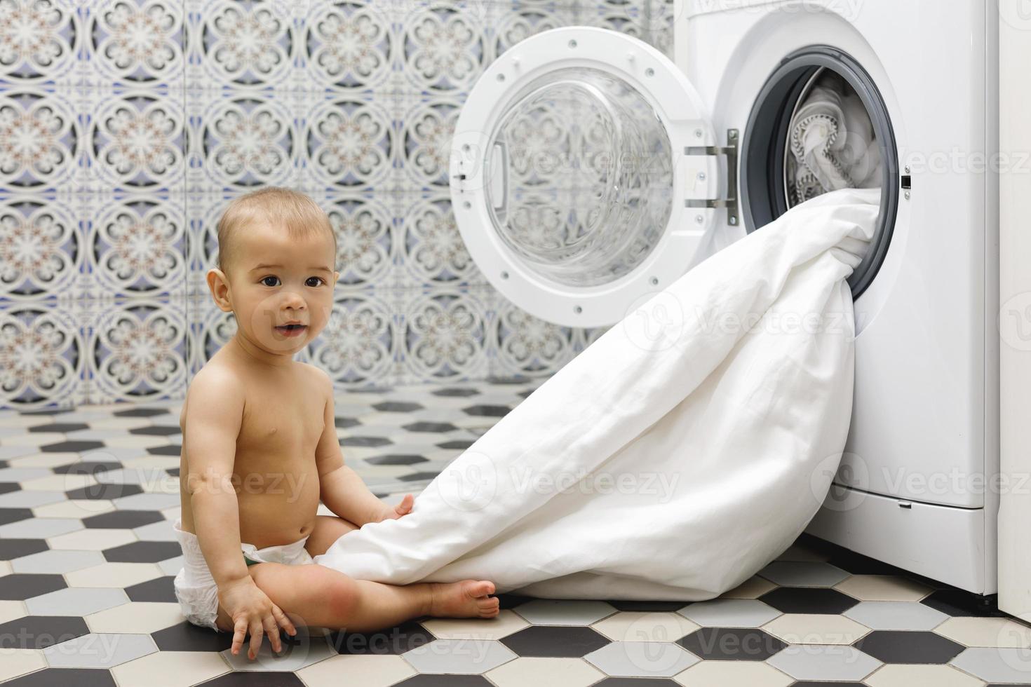 schattig baby jongen naast de het wassen machine foto