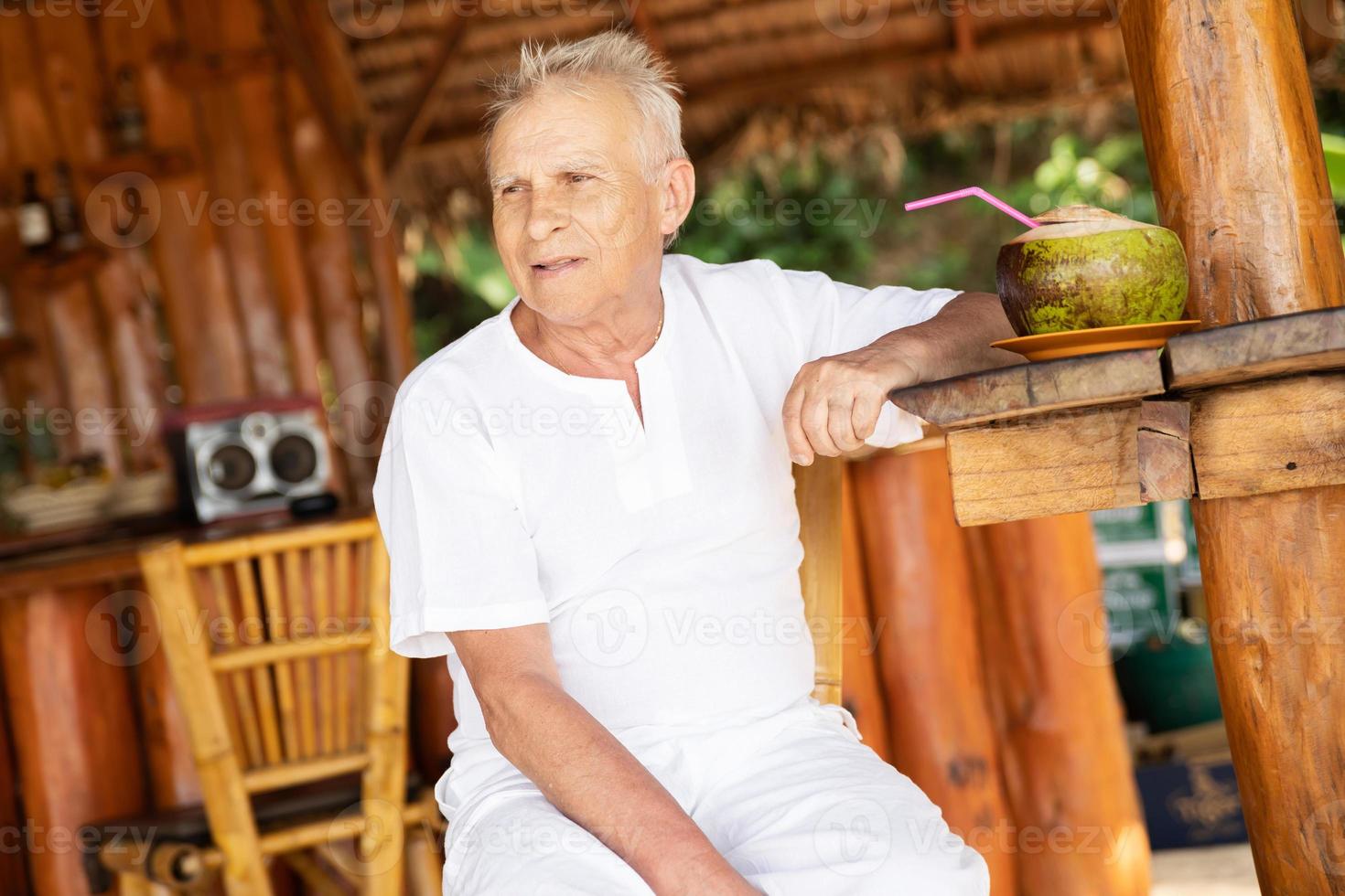 gelukkig senior Mens is drinken een kokosnoot water in de strand bar foto