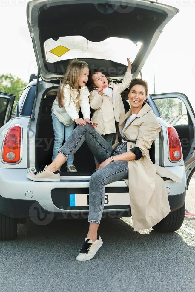 jong moeder en haar aanbiddelijk dochters zittend in een auto kofferbak. foto