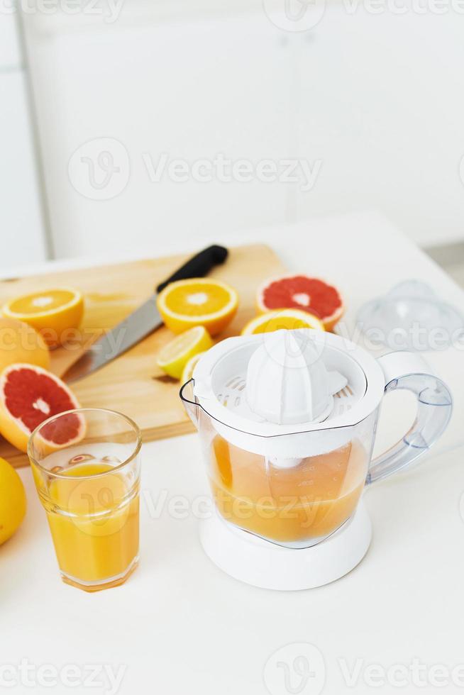 glas van oranje sap, citrus sapcentrifuge en divers citrus fruit Aan keuken tafel foto