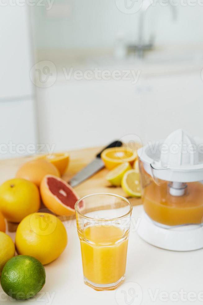 glas van oranje sap, citrus sapcentrifuge en divers citrus fruit Aan keuken tafel foto