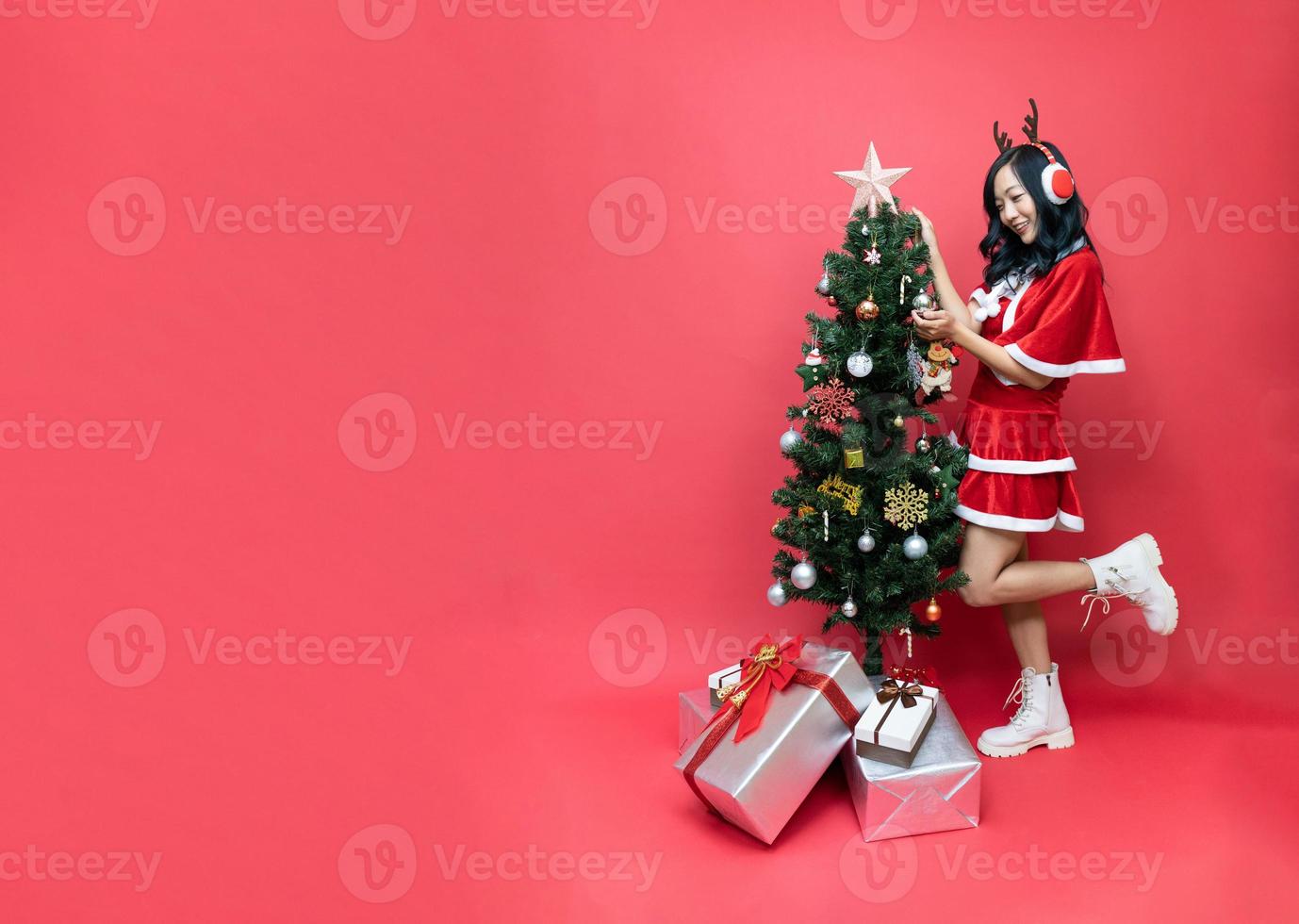 jong Azië vrouw in rood santy kostuum versieren de Kerstmis boom. nieuw jaar viering. Kerstmis vooravond. foto
