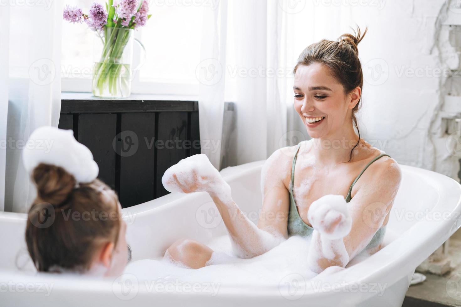 jong moeder vrouw en weinig tween meisje dochter hebben pret in bad met schuim Bij huis foto