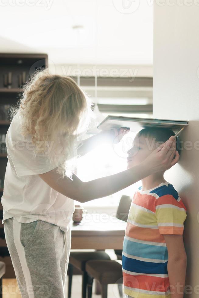 moeder speels meten de hoogte van haar zoon Bij huis foto