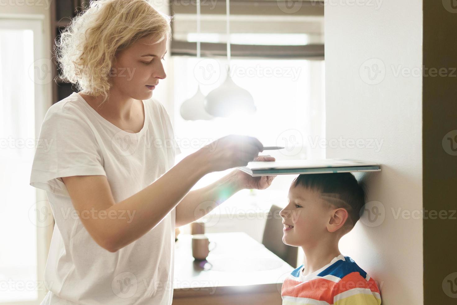 moeder speels meten de hoogte van haar zoon Bij huis foto