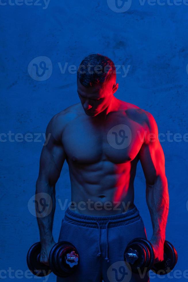 gespierd bodybuilder Mens oefenen met halters in kleurrijk neon licht foto