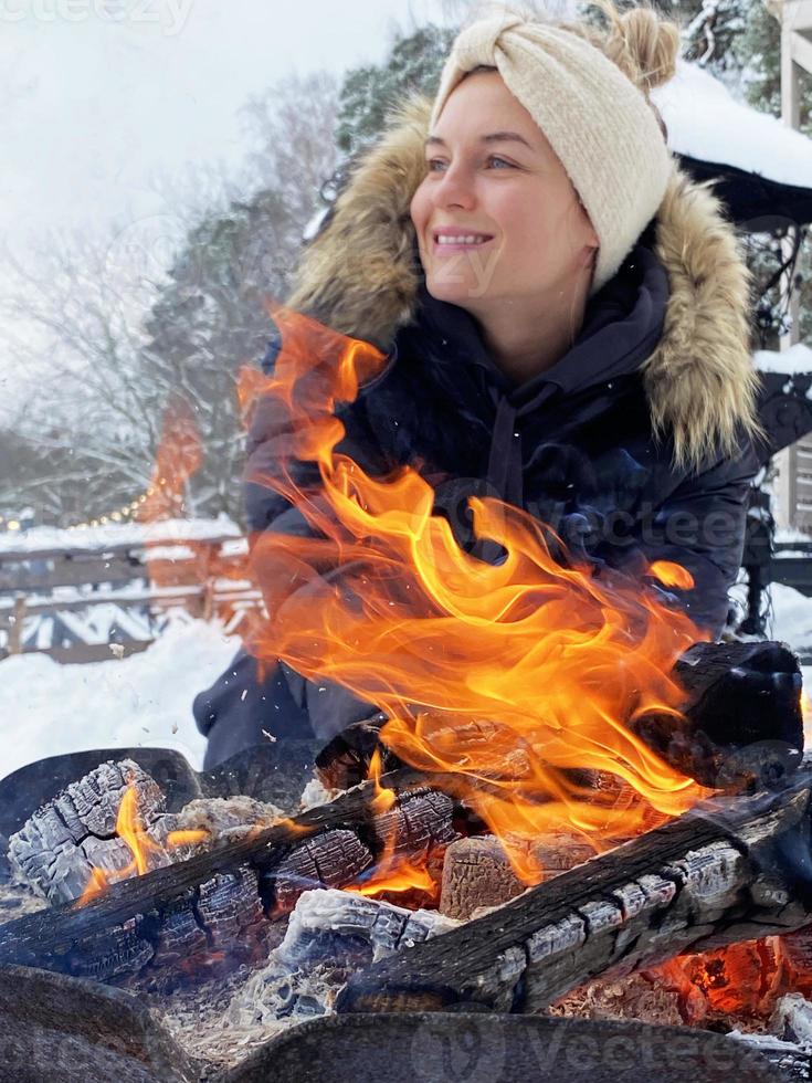 jong vrouw opwarming omhoog door de brand pit gedurende verkoudheid winter dag foto