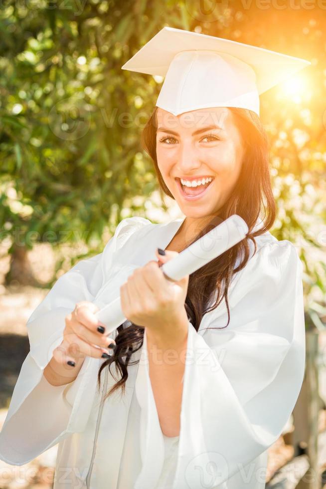 afstuderen gemengd ras meisje in pet en japon met diploma foto