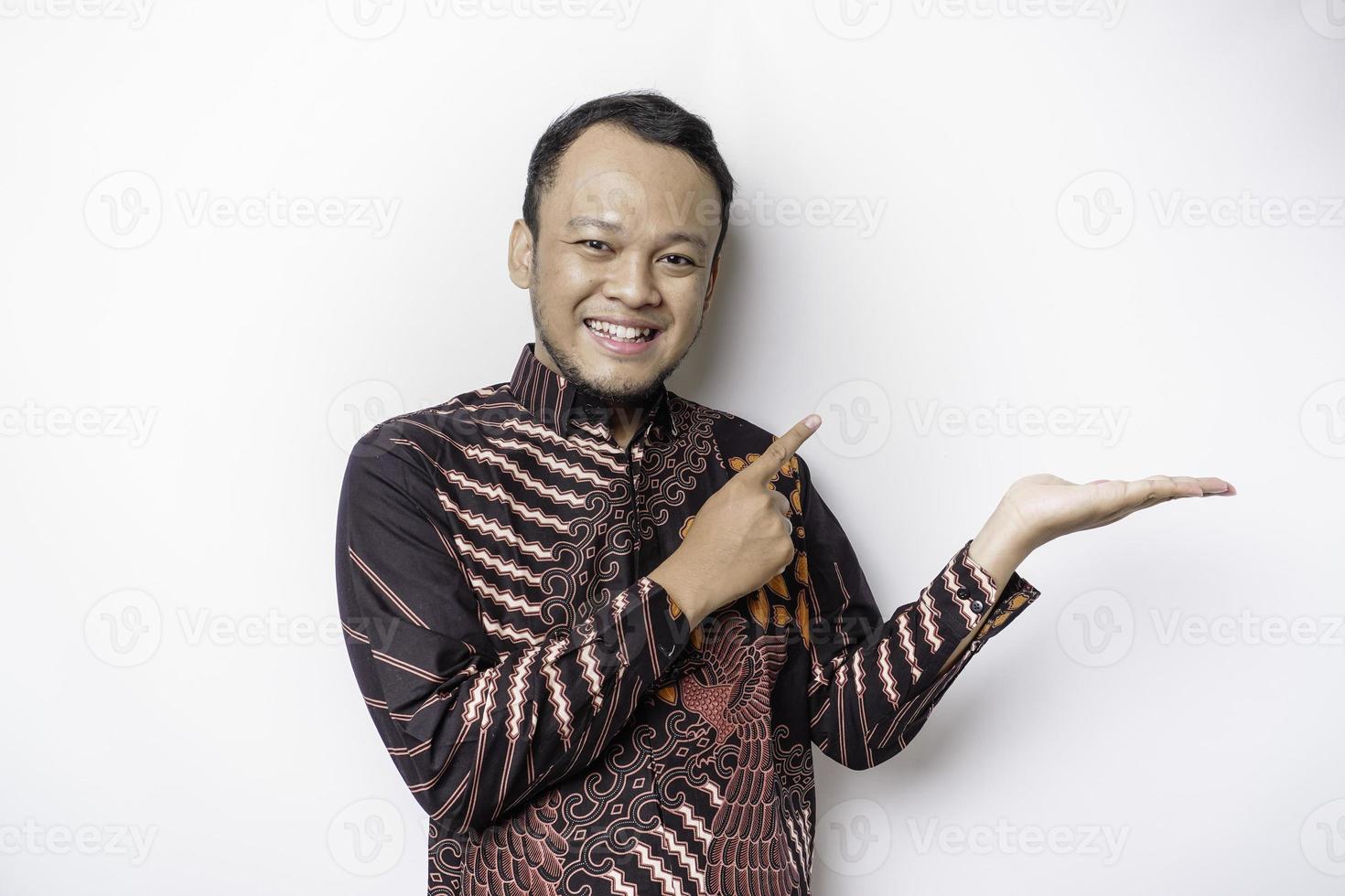 opgewonden Aziatisch Mens vervelend batik overhemd richten Bij de kopiëren ruimte naast hem, geïsoleerd door wit achtergrond foto