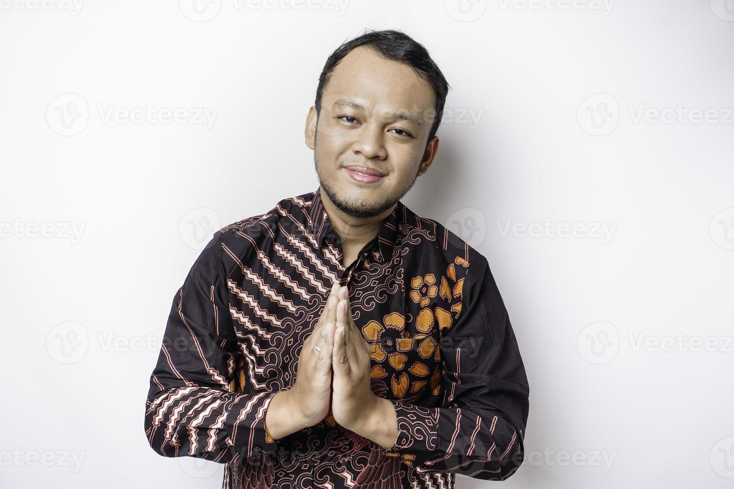 glimlachen jong Aziatisch Mens vervelend batik shirt, gebaren traditioneel groet geïsoleerd over- wit achtergrond foto