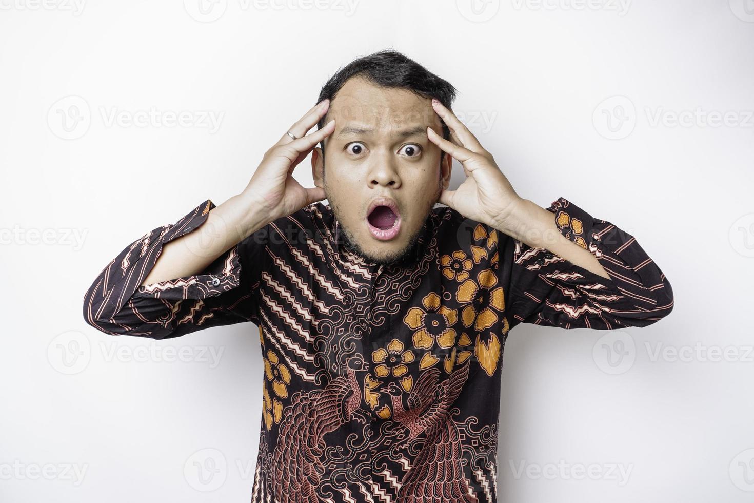 geschokt Indonesisch Mens vervelend batik overhemd en op zoek omhoog, geïsoleerd door wit achtergrond foto