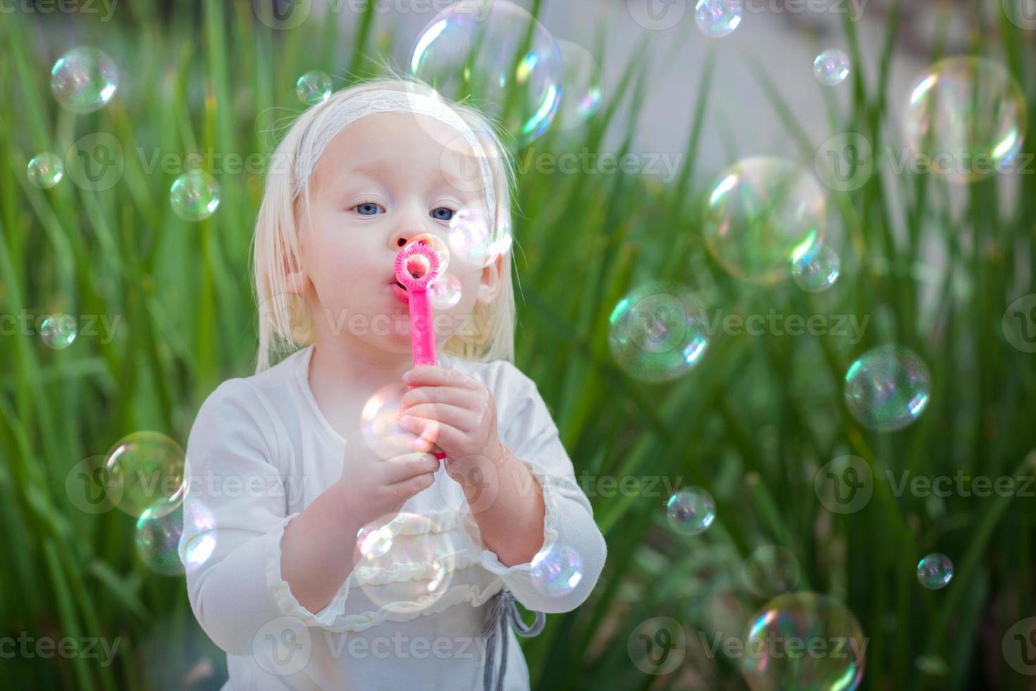 aanbiddelijk weinig meisje zittend Aan bank hebben pret met blazen bubbels buiten. foto