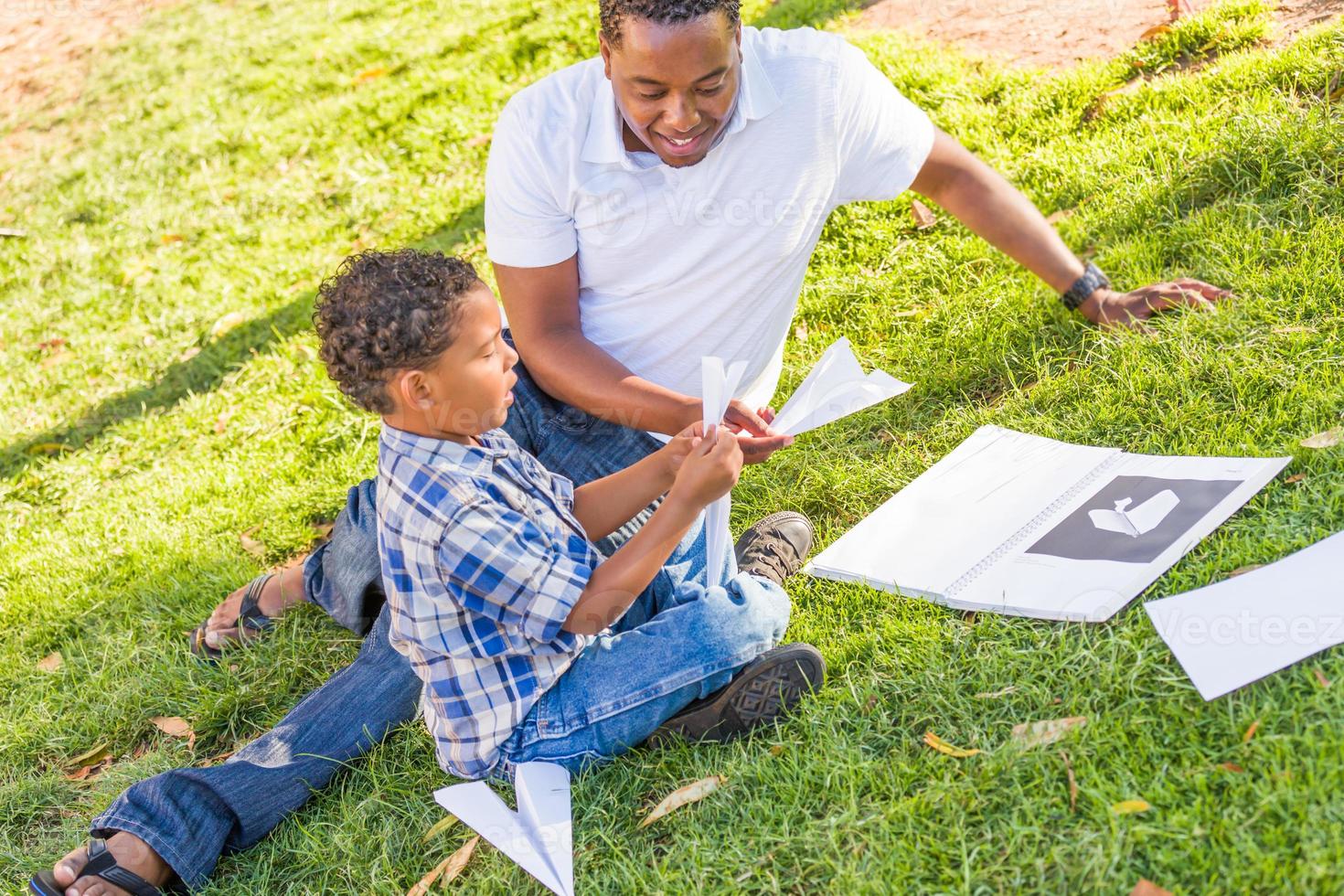 gelukkig Afrikaanse Amerikaans vader en gemengd ras zoon spelen met papier vliegtuigen in de park foto
