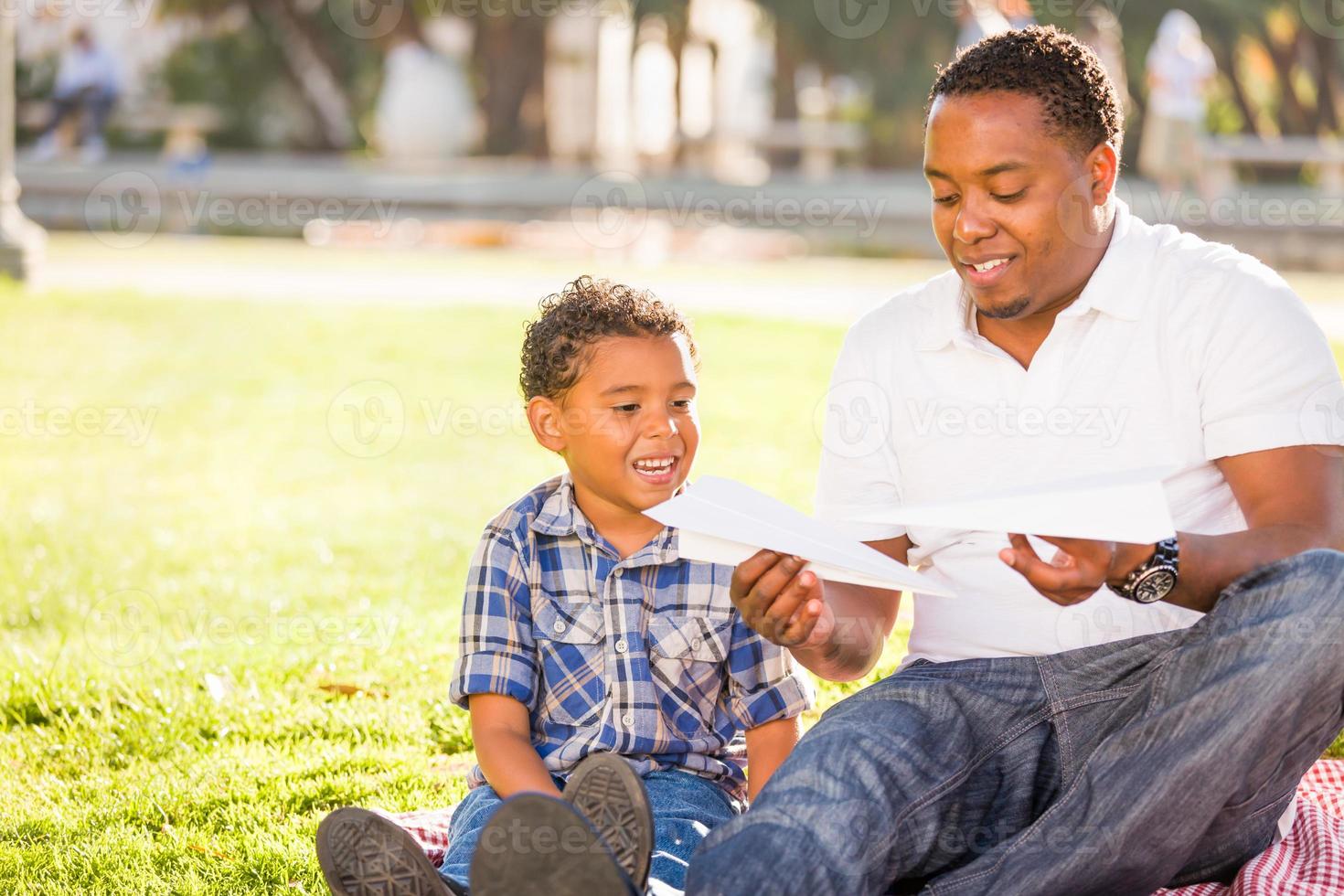 gelukkig Afrikaanse Amerikaans vader en gemengd ras zoon spelen met papier vliegtuigen in de park foto