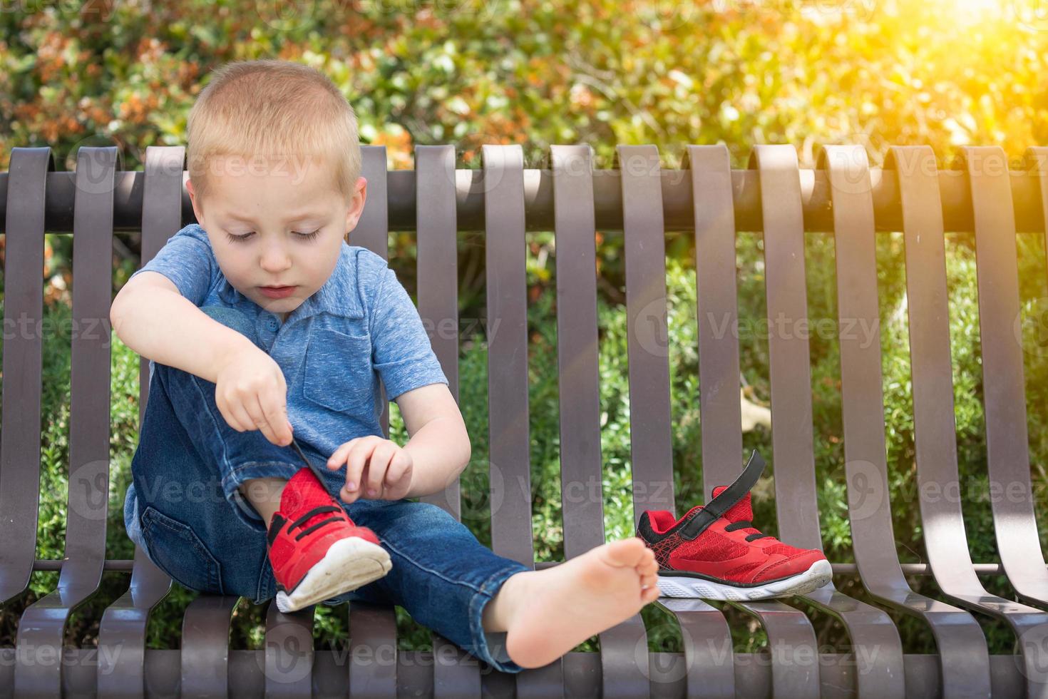 jong jongen zittend Aan een bank zetten Aan zijn schoenen Bij de park foto