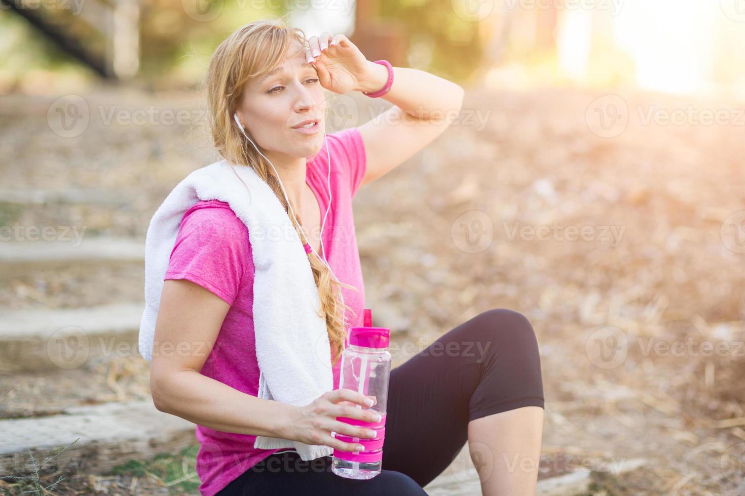 jong fit volwassen vrouw buitenshuis met handdoek en water fles in training kleren luisteren naar muziek- met oortelefoons. foto