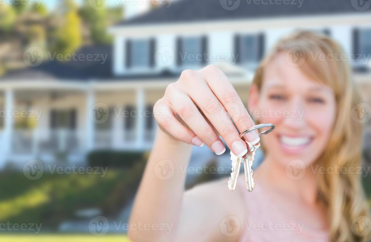 opgewonden vrouw Holding huis sleutels in voorkant van mooi hoor nieuw huis. foto