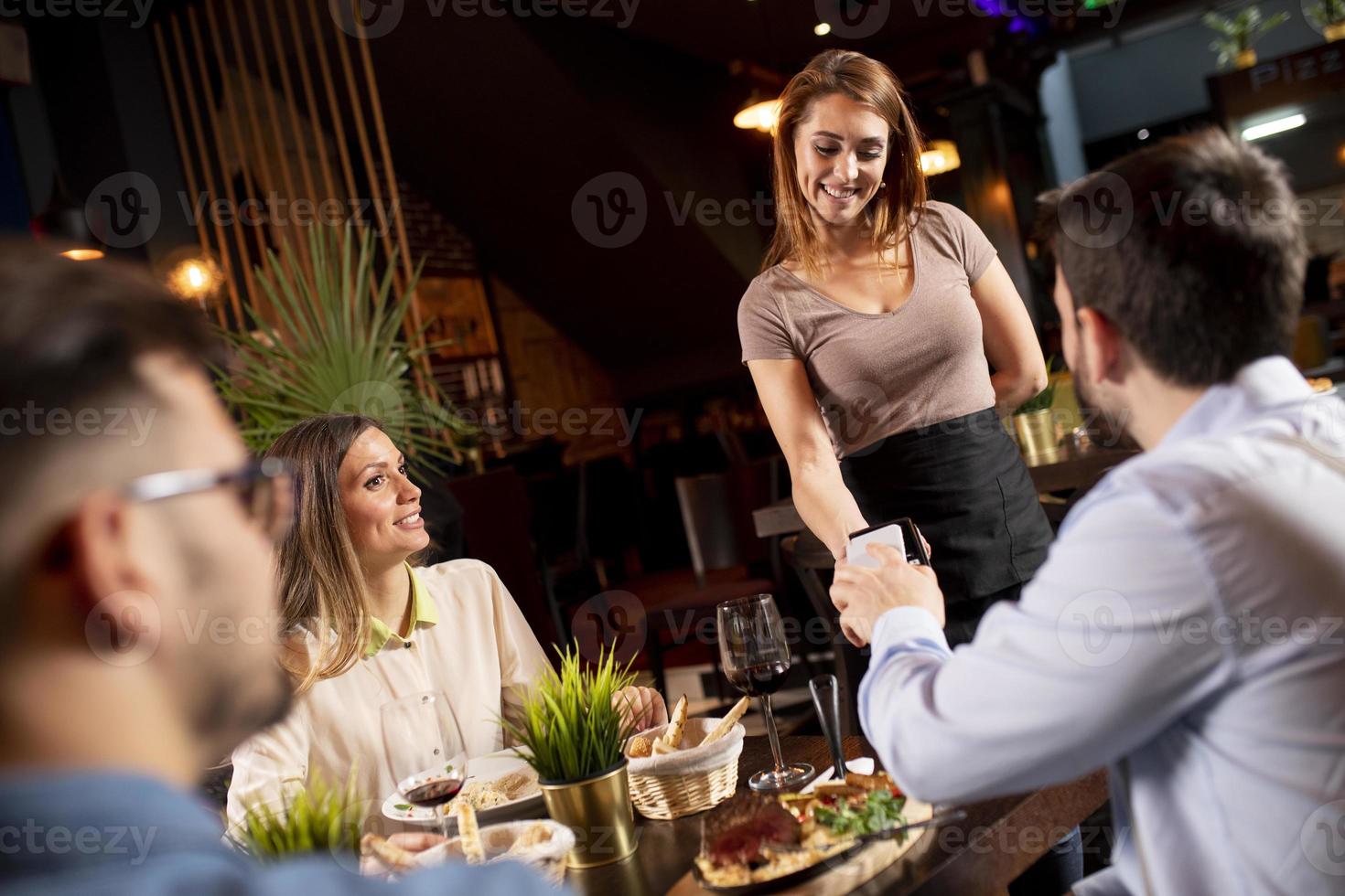 jong Mens betalen contactloos met mobiel telefoon in de restaurant foto