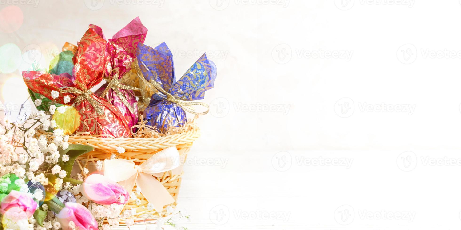 Pasen banier met mand van eieren verpakt in kleurrijk papier, bloemen, bokeh lichten. kopiëren ruimte. foto