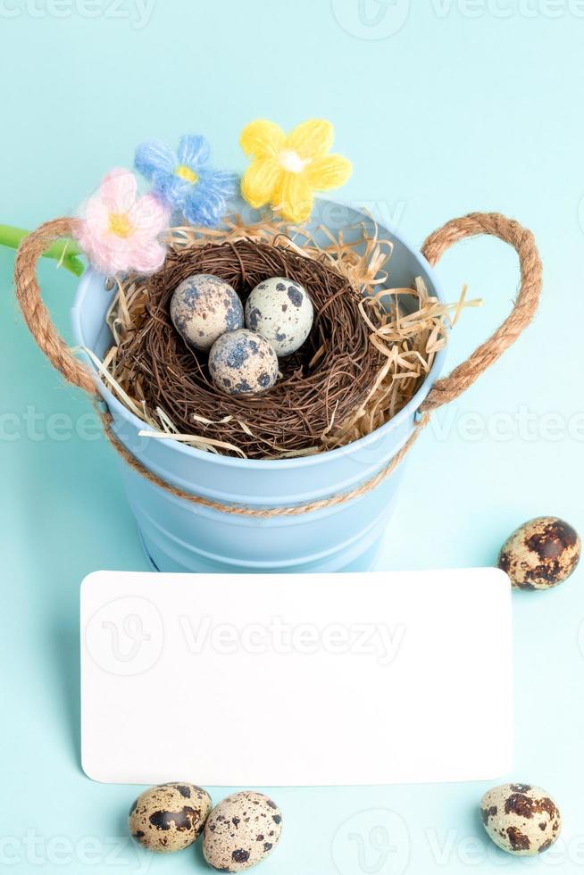 Pasen groet kaart met kwartel eieren, leeg wit Opmerking, gebreid bloemen Aan pastel blauw achtergrond. foto