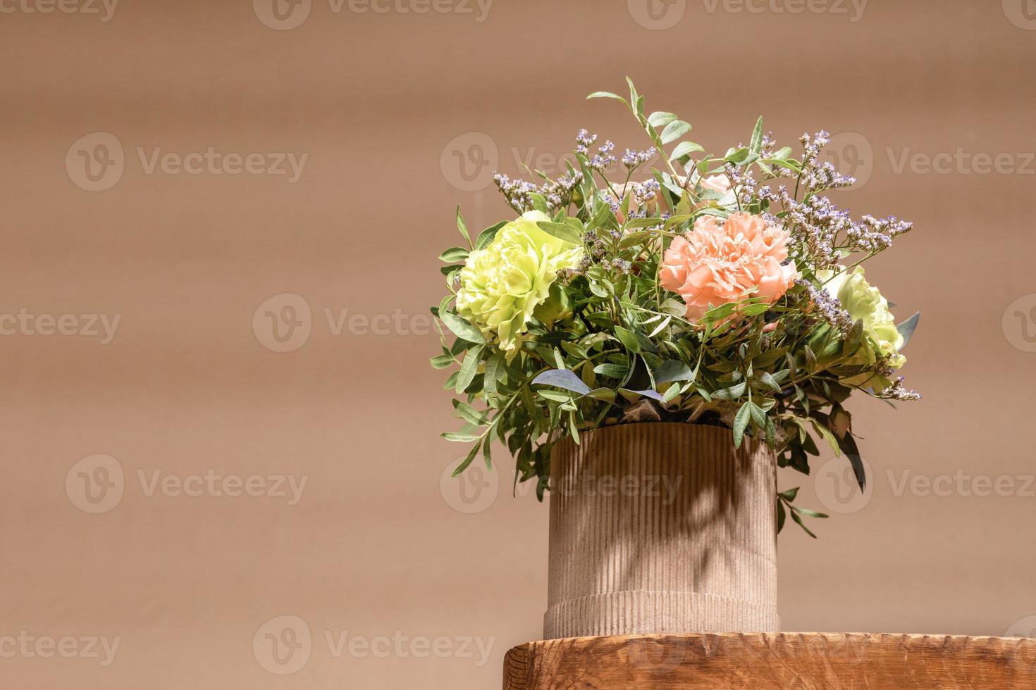 ecologisch samenstelling met bloemen boeket in diy karton vaas staand Aan oud houten tafel Aan beige met schaduwen. foto