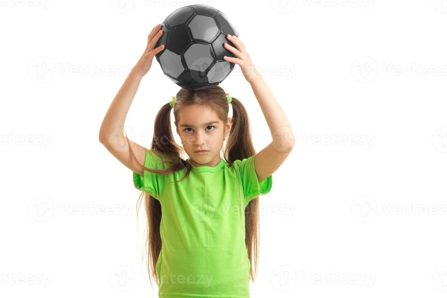 charmant weinig meisje Holding een voetbal bal Aan haar hoofd foto