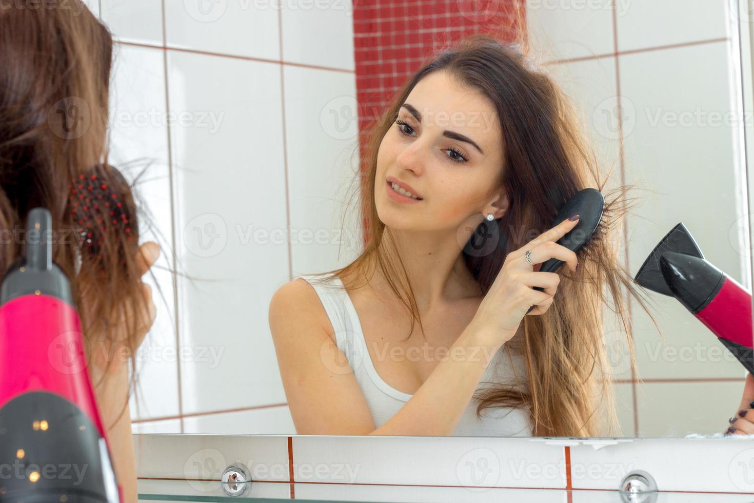 schattig jong meisje droogt haar- in voorkant van een spiegel foto