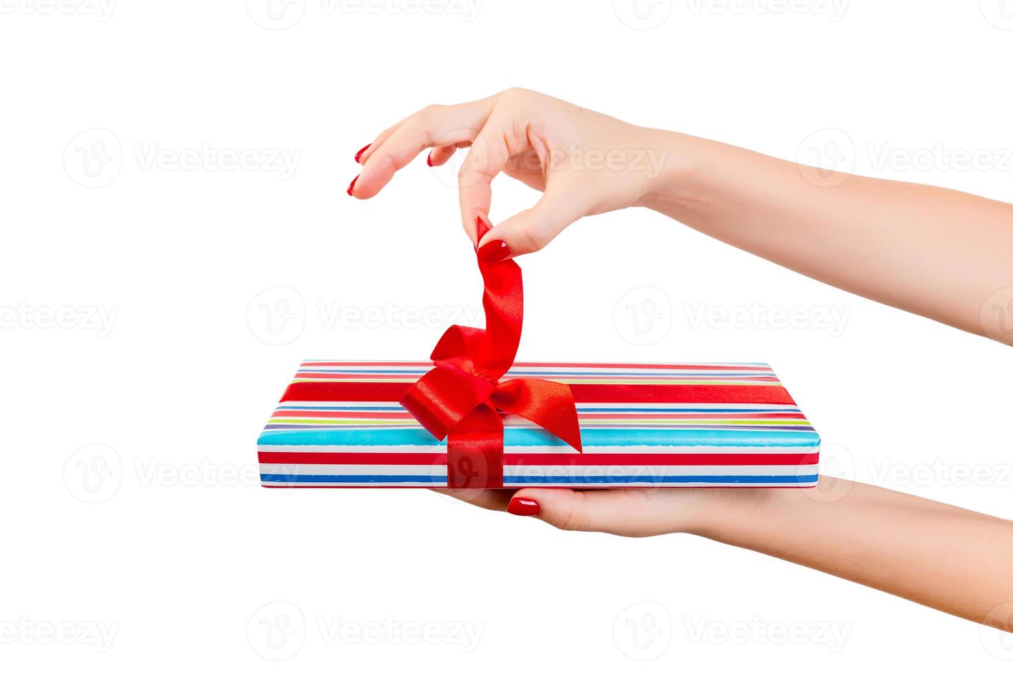 vrouw handen losmaken verpakt Kerstmis of andere vakantie handgemaakt Cadeau in gekleurde papier met rood lintje. geïsoleerd Aan wit achtergrond, top visie. dankzegging geschenk doos concept foto