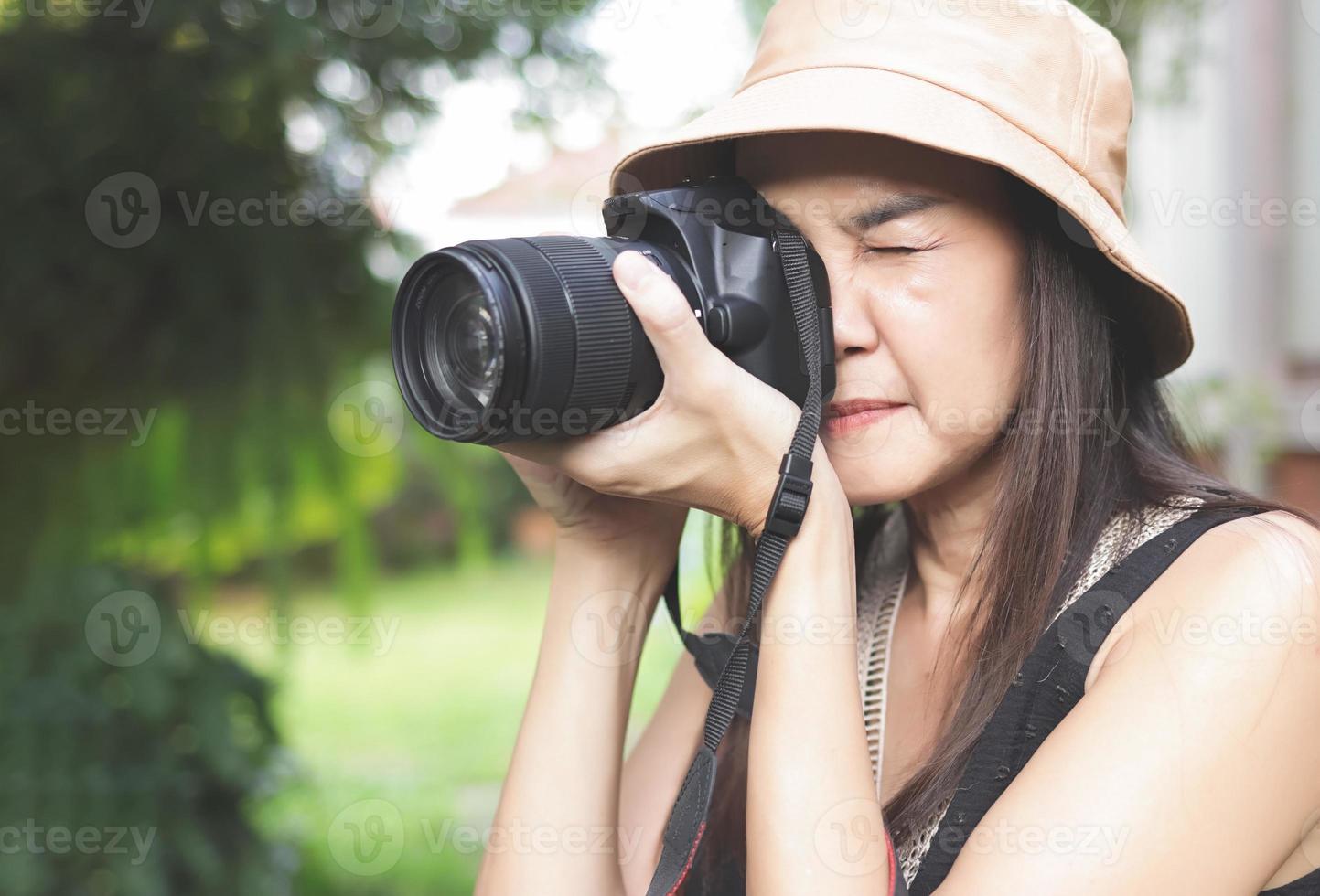 Aziatisch vrouw vervelend hoed en mouwloos top nemen foto's in de park met dslr camera. foto